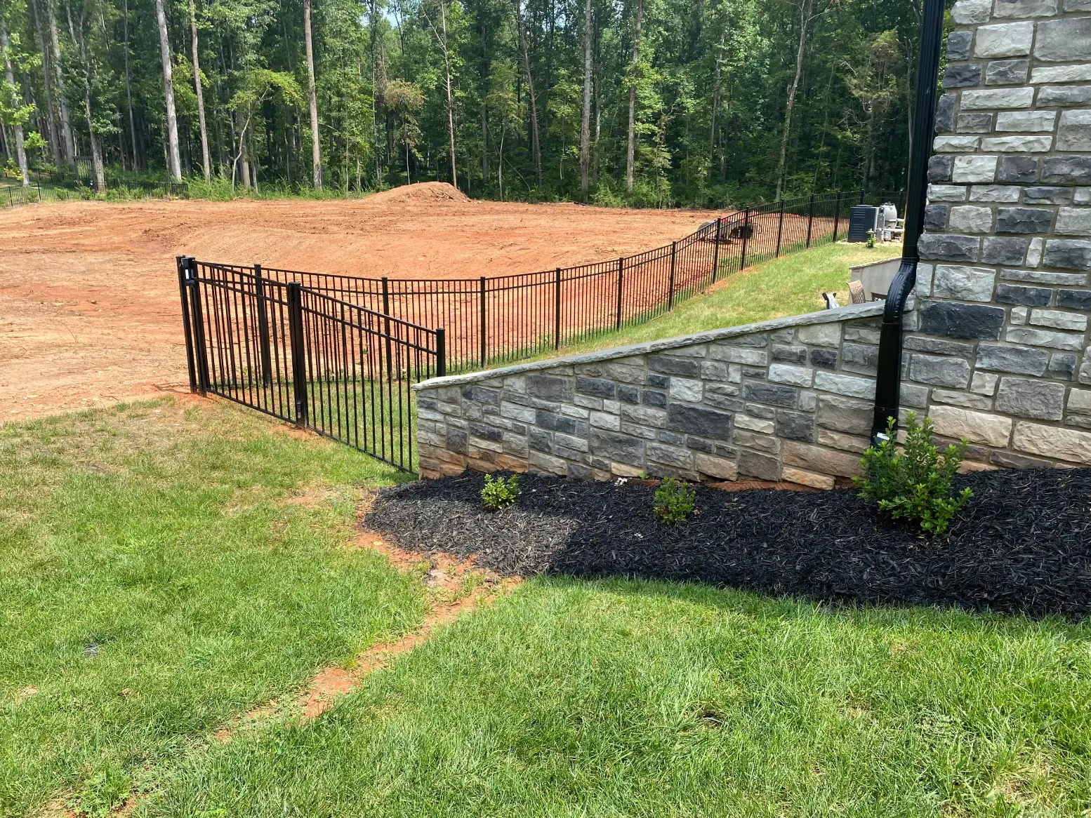 A fence that is in the grass near some dirt.