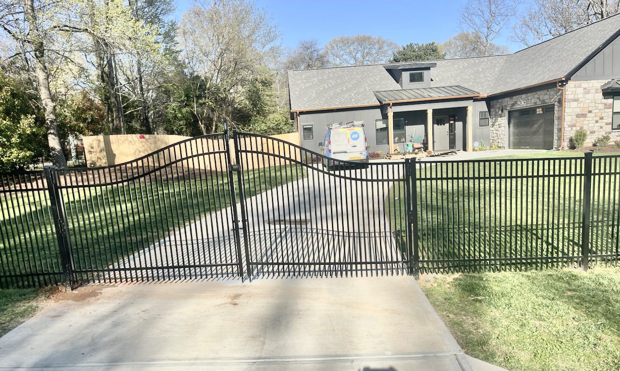 A driveway with two gates and a house in the background.