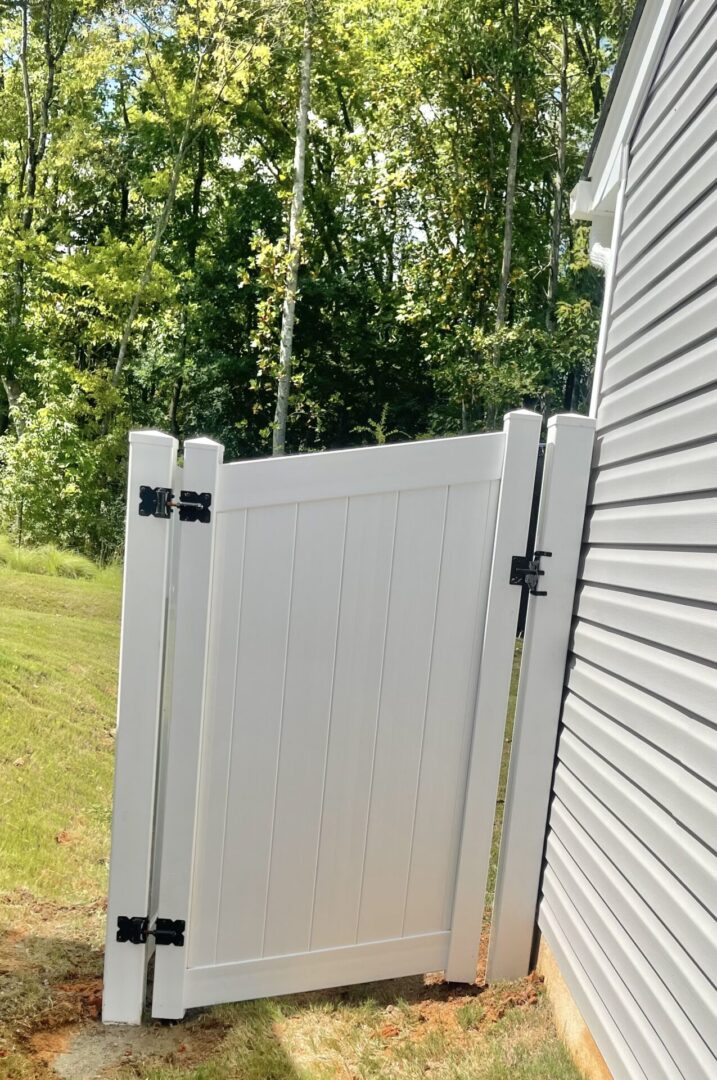 A white gate is open on the side of a house.