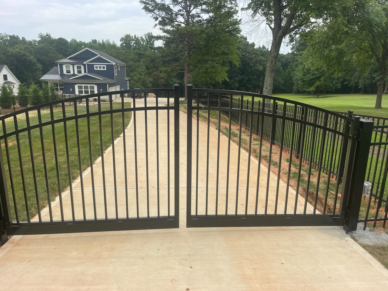 A driveway with two gates open and trees in the background.